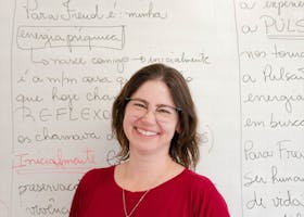 A cheerful female teacher standing in front of a whiteboard with handwriting.